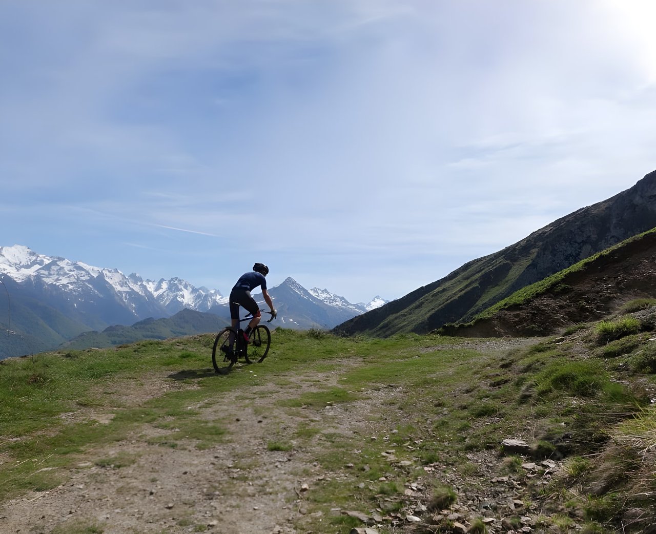 Gravel rider on a grassy mountain track with snow-capped peaks behind, on an Escape To The Pyrenees tour.
