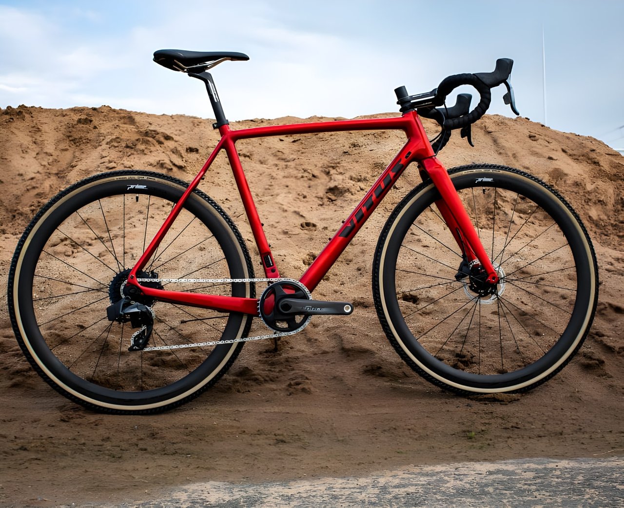 Red Vitus Energie Carbon cyclocross bike with SRAM groupset and tan-wall tyres against a pile of sand.