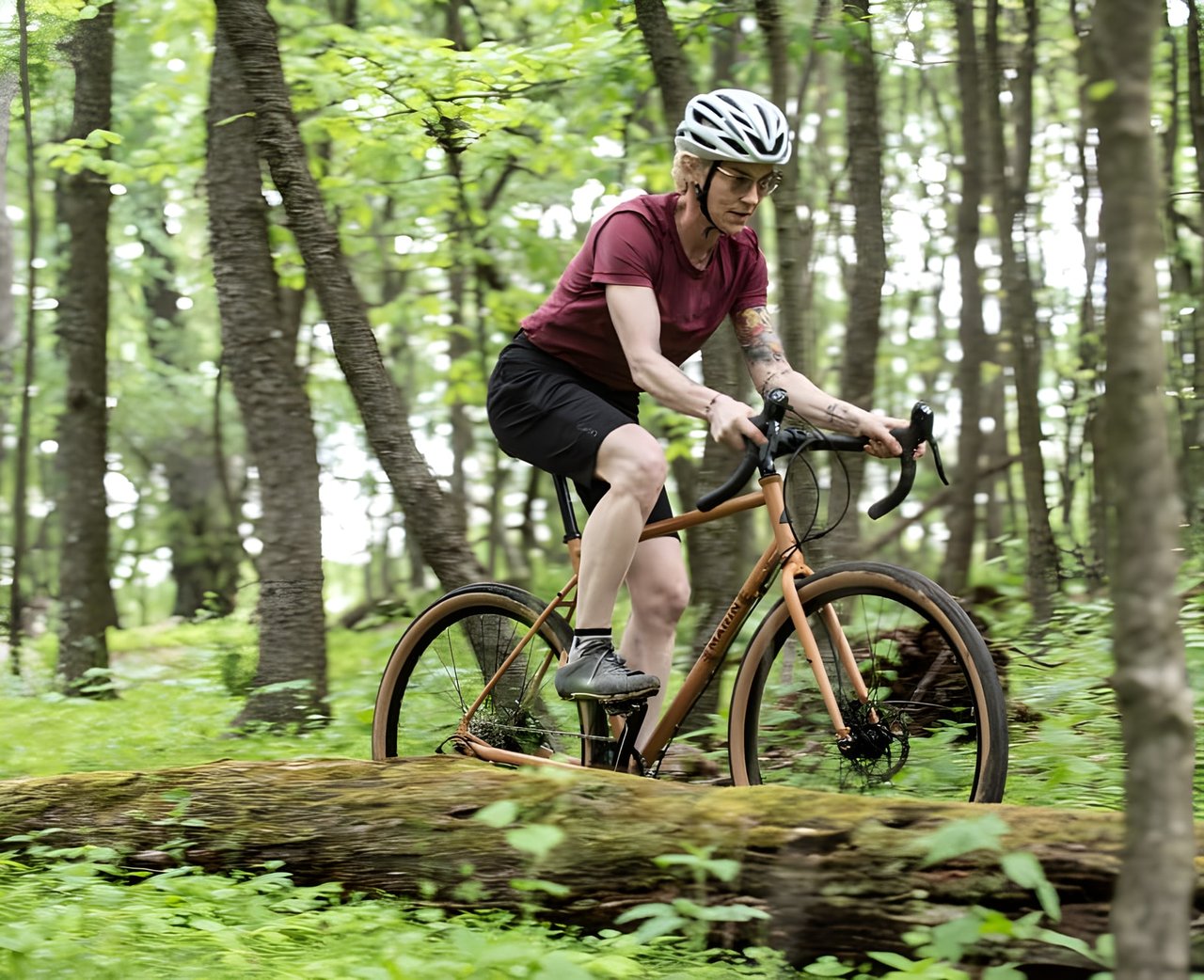A rider on a Marin gravel bike crosses a fallen log on a wooded trail.