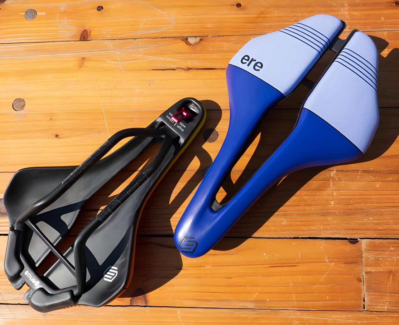 ERE Research Genus saddles, one black carbon underside and one blue and lilac top, on a wooden table.