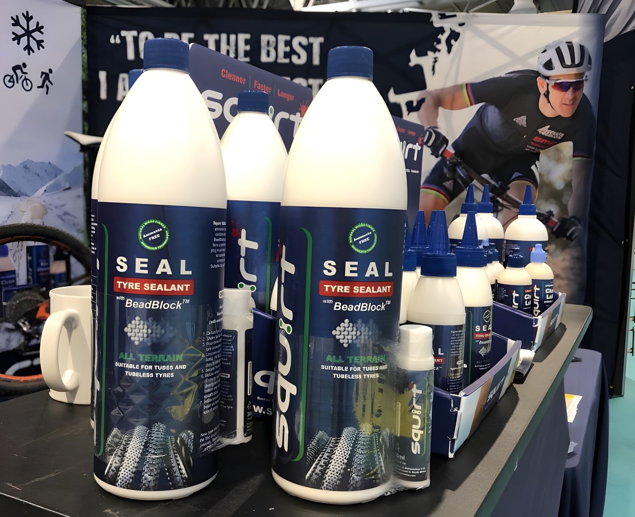 Bottles of Squirt SEAL tubeless tyre sealant with BeadBlock on a display table, a rider pictured on the banner behind.