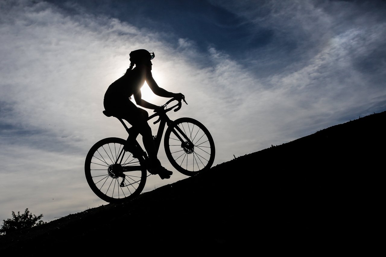 Silhouetted rider climbs a slope against the sun at Gravel Origins 83, part of the Roc d'Azur festival in France.