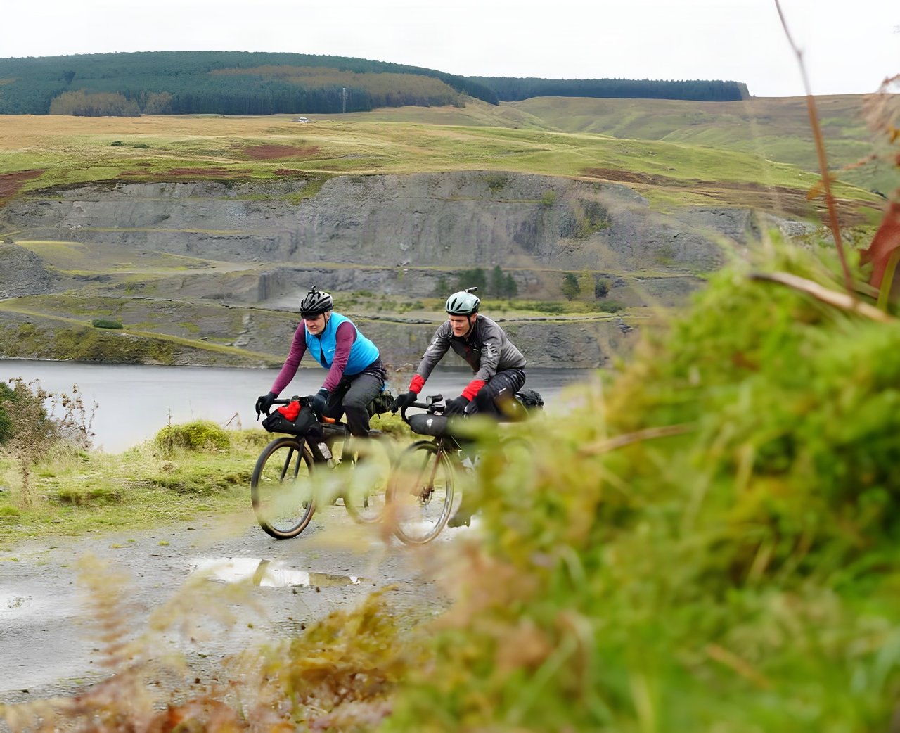 Two riders with bikepacking bags on a gravel track beside a reservoir in Mid Wales, on the Wildcat 100 route.