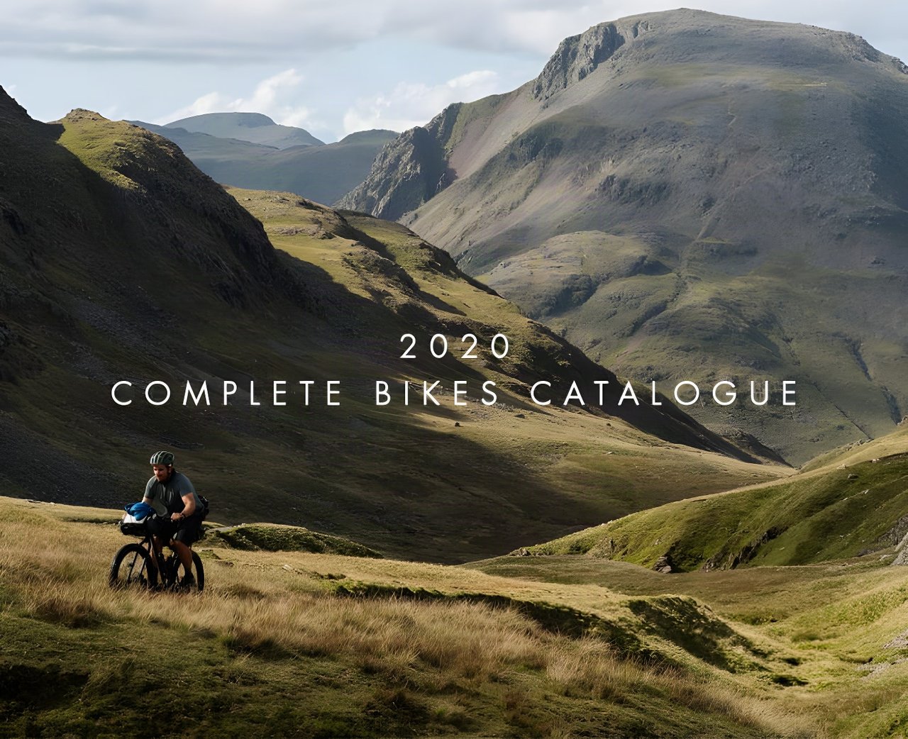 Bombtrack 2020 Complete Bikes Catalogue cover: a bikepacker rides a loaded bike through grassy mountain valleys.