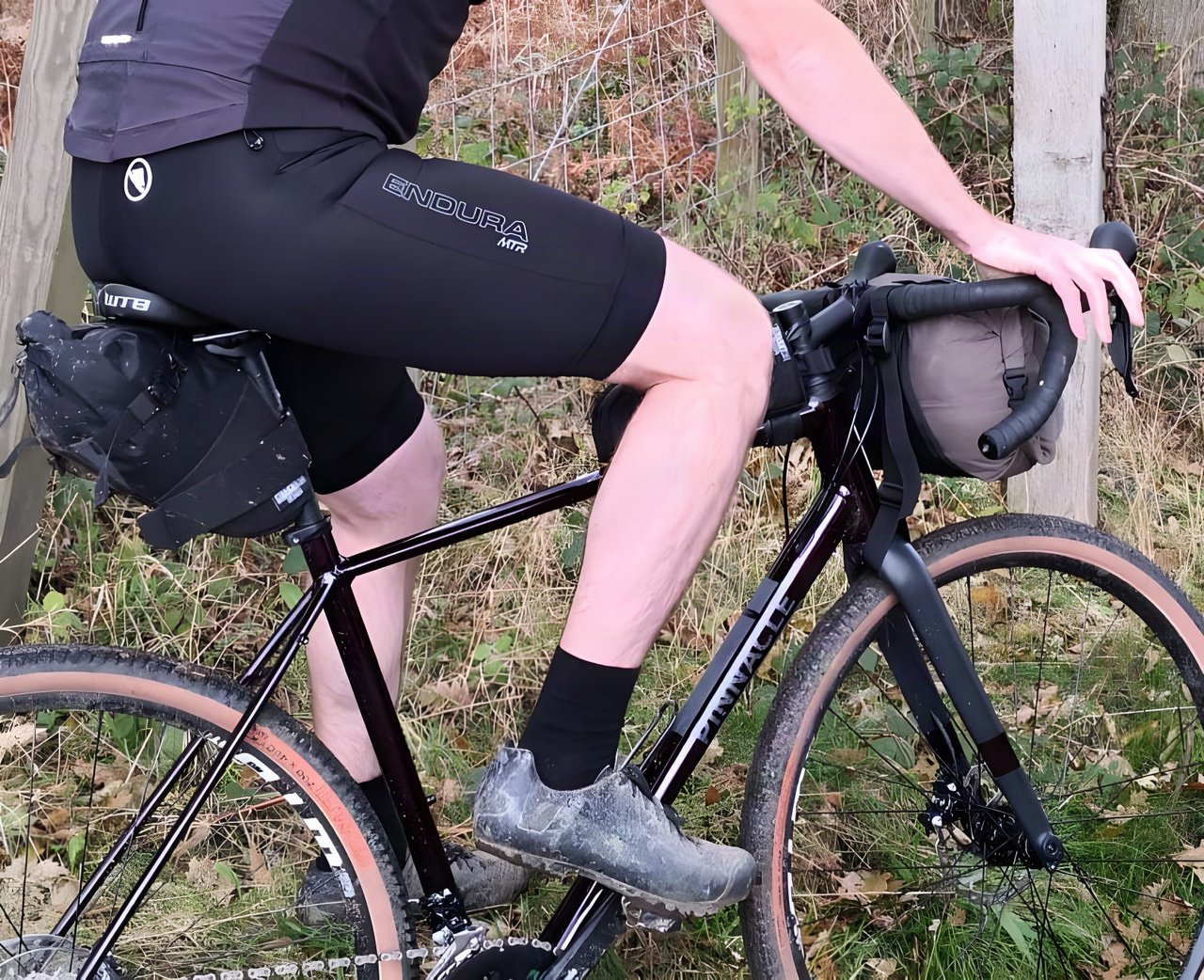 Close-up of the Endura MTR Spray bib-shorts on a rider sat on a black Pinnacle gravel bike with bikepacking bags.