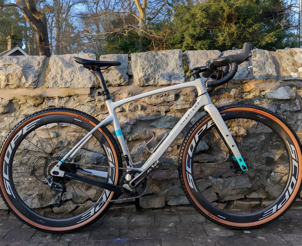 Scope R4A wheels on a grey and teal Chapter2 gravel bike leaning against a stone wall.
