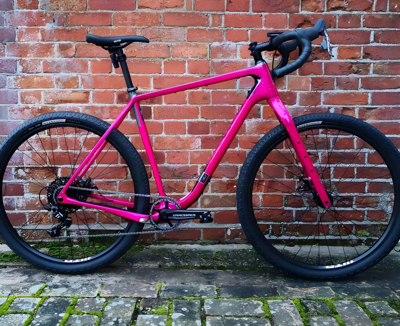 Hot pink 2020 Salsa Cutthroat Apex 1 against a red brick wall, side view of the bike bound for the Atlas Mountain Race.
