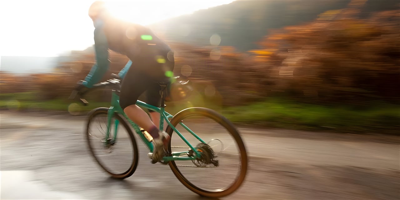Rider on a green gravel bike blurs past autumn trees in low sun, key image for the Sonder Winter Gravel Series at Gateshead.