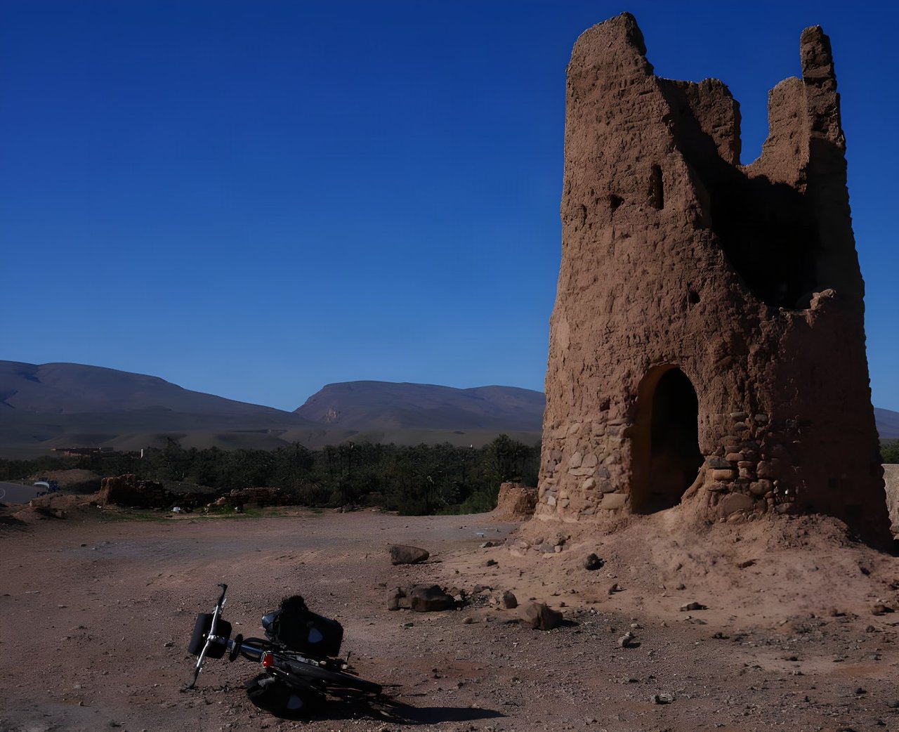 A loaded bikepacking bike lies beside a ruined mud-brick kasbah tower in Morocco, where the Atlas Mountain Race is run.