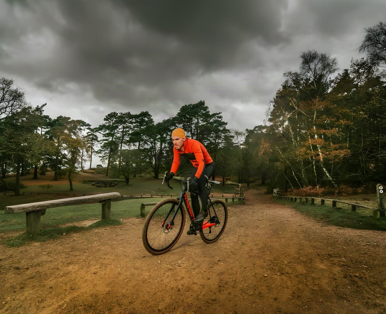 Rider in an orange jacket on the Pearson Off Grid carbon gravel bike on a woodland track under dark cloud.