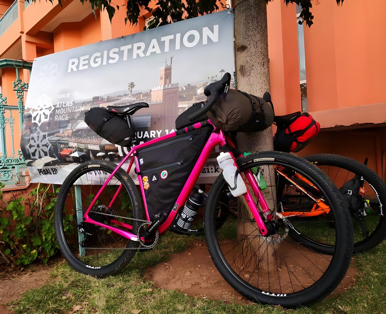 Pink Salsa Cutthroat with bikepacking bags parked by the Atlas Mountain Race registration banner in Marrakech.