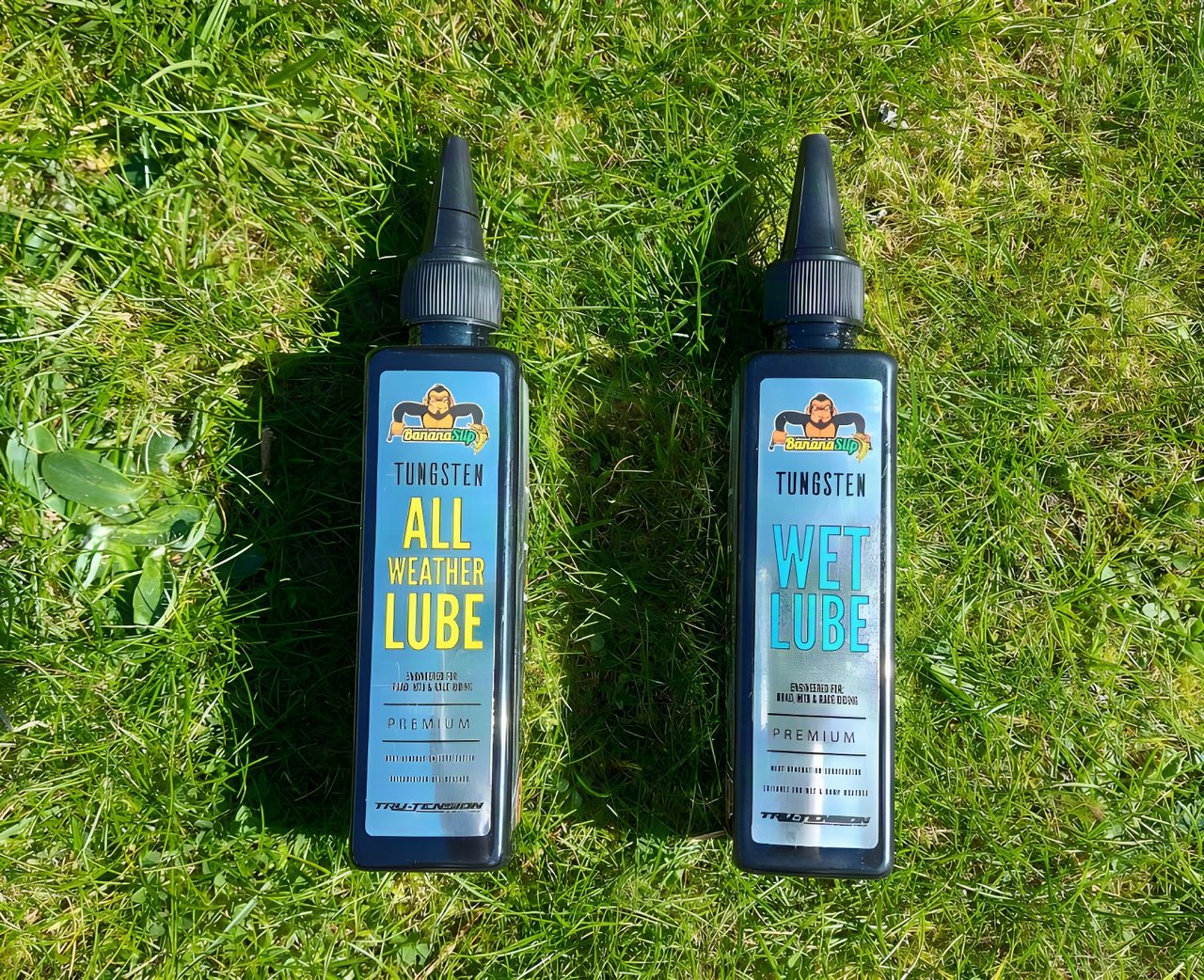 Tru-Tension BananaSlip Tungsten all-weather and wet chain lube bottles side by side on grass.