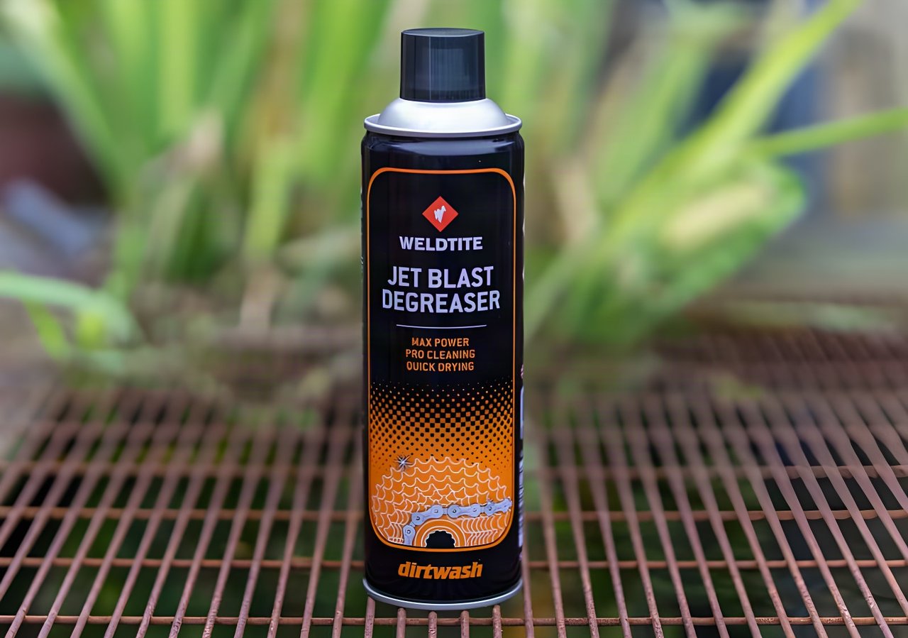 Weldtite Jet Blast Degreaser aerosol can standing on a rusty metal grille with garden plants behind.
