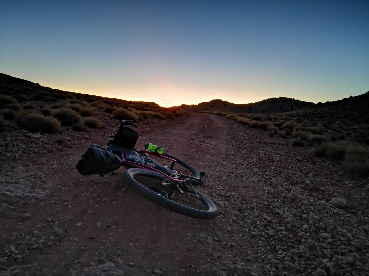 Loaded bikepacking bike lying on a stony track in arid scrub at twilight, an ultra-distance scene for DotWatcher fans.