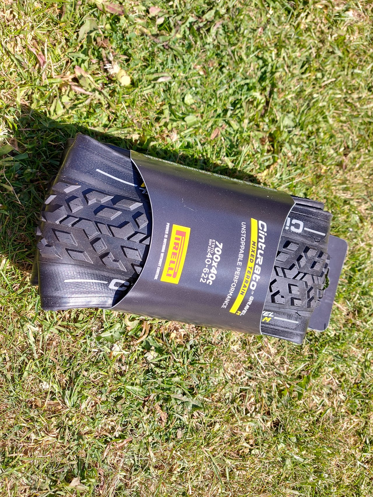 Pirelli Cinturato Gravel M 700x40c folded tyre in its packaging, lying on grass.