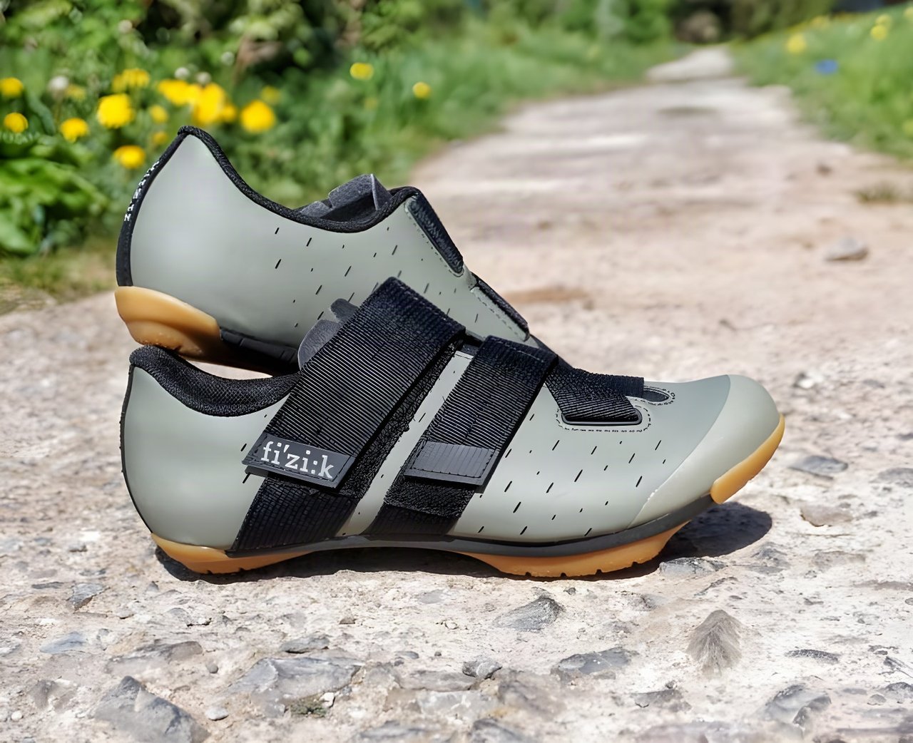 Fizik Terra Powerstrap X4 gravel shoes in khaki with gum soles and black velcro straps, on a dirt track.