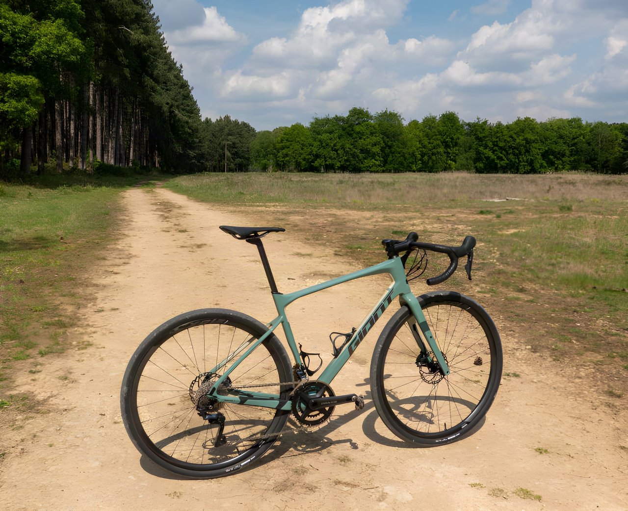 Giant Revolt Advanced 0 carbon gravel bike in teal on a sandy track beside open heath and woodland.