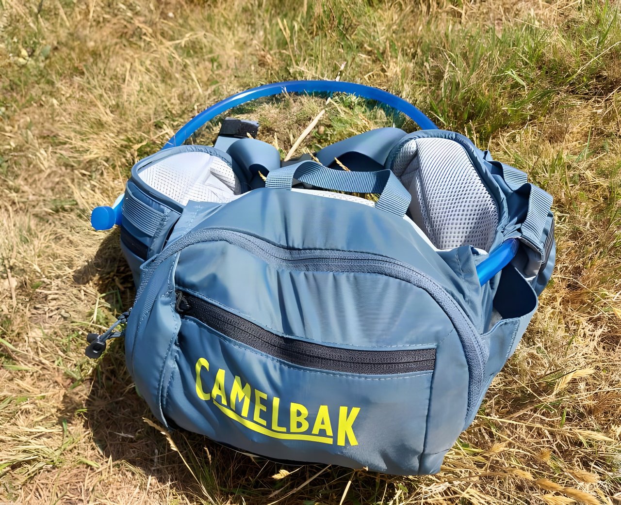 Camelbak Repack LR 4 hydration waistpack in blue lying on dry grass, with the hose looped over the top.