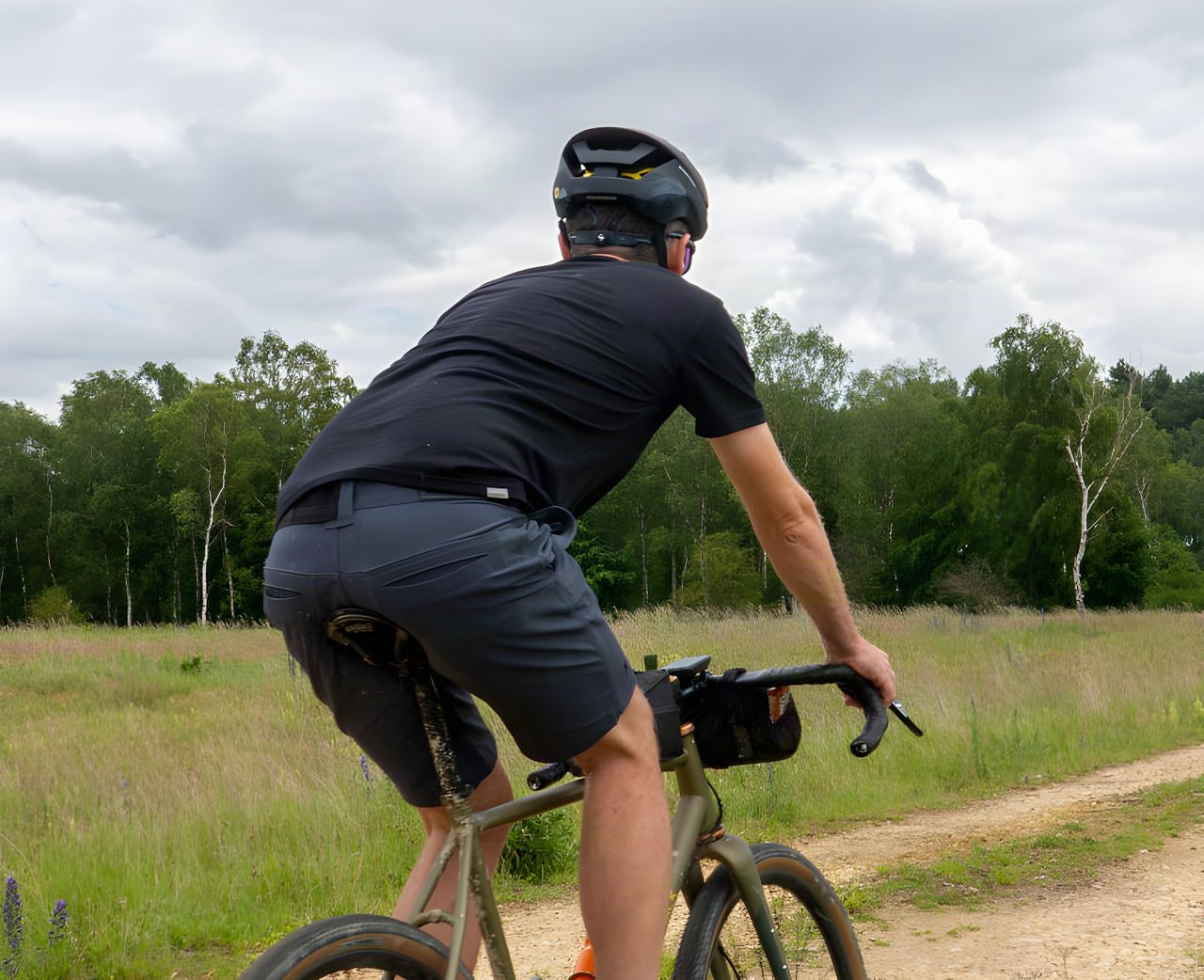 Rider in Chrome Industries Folsom Short 2.0 shorts pedals a gravel bike along a sandy track through open grassland.