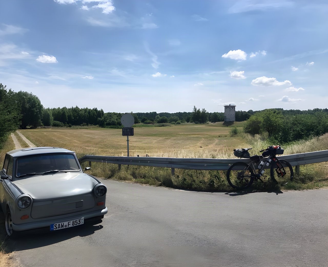 Trabant and loaded bikepacking bike beside a former East German watchtower on the Grenzsteintrophy route.