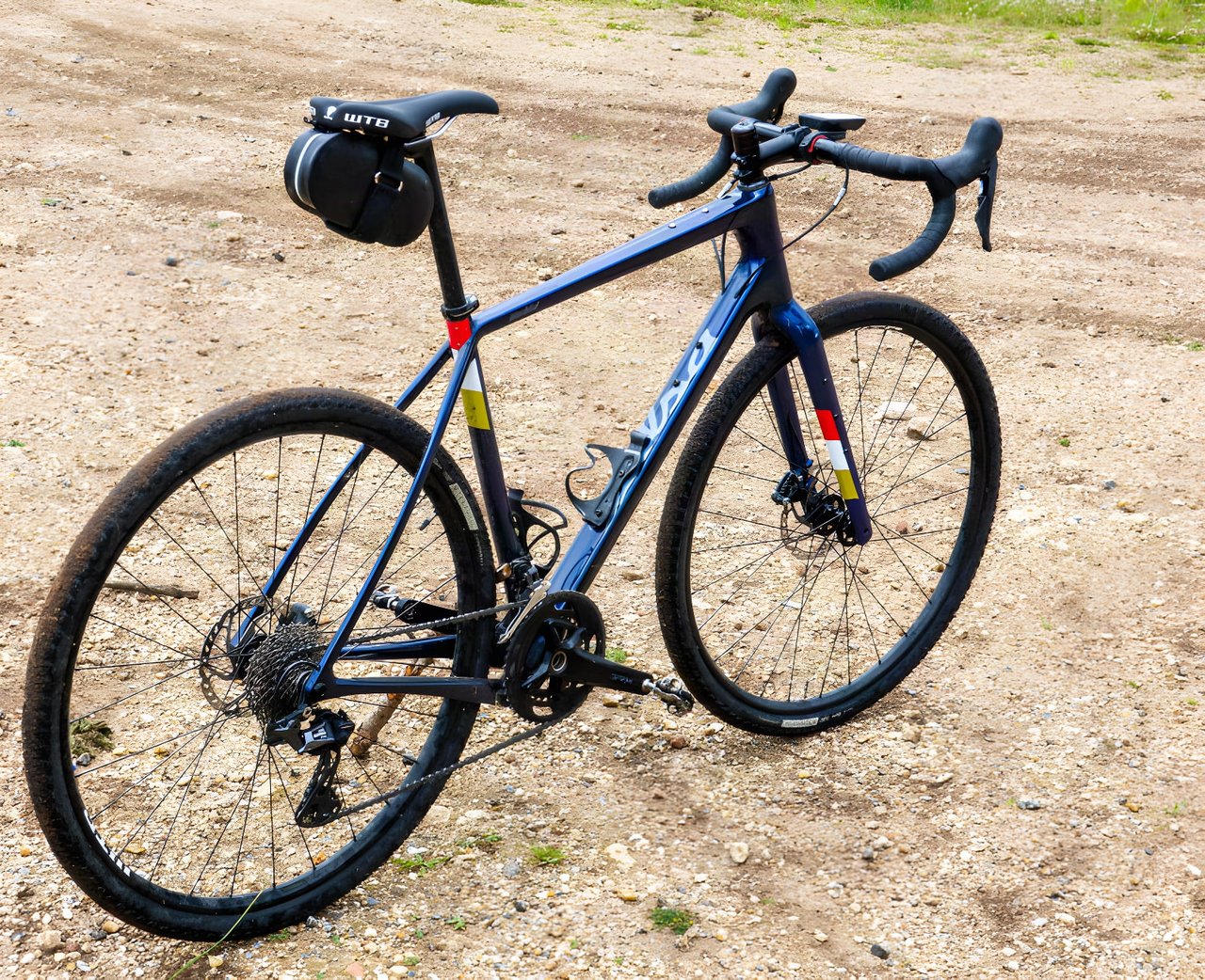 Blue Salsa Warbird GRX 600 gravel bike with a saddle bag, three-quarter view on a dirt track.