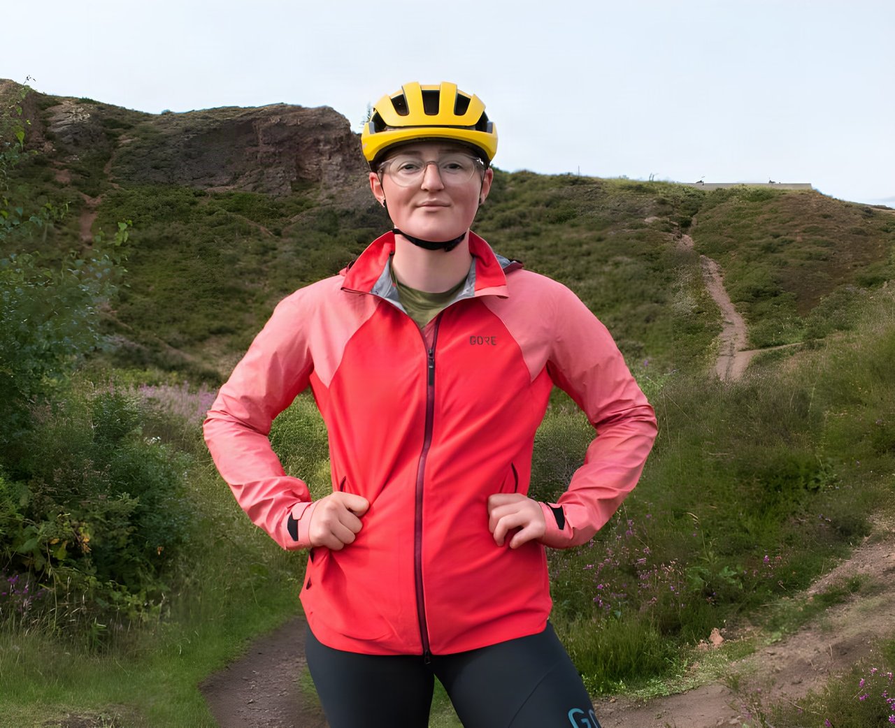 Katherine Moore in the GORE C5 Women's Infinium Hybrid Hooded Jacket and a yellow helmet on a heathland trail.