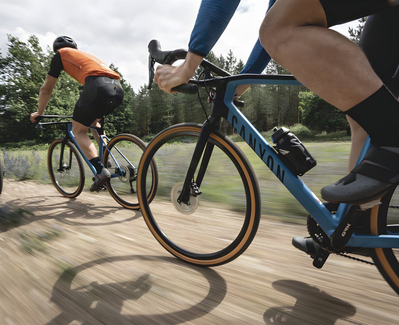 Two riders on Canyon gravel bikes with tan-wall tyres race along a dirt track, promoting the King's Cup gravel festival.