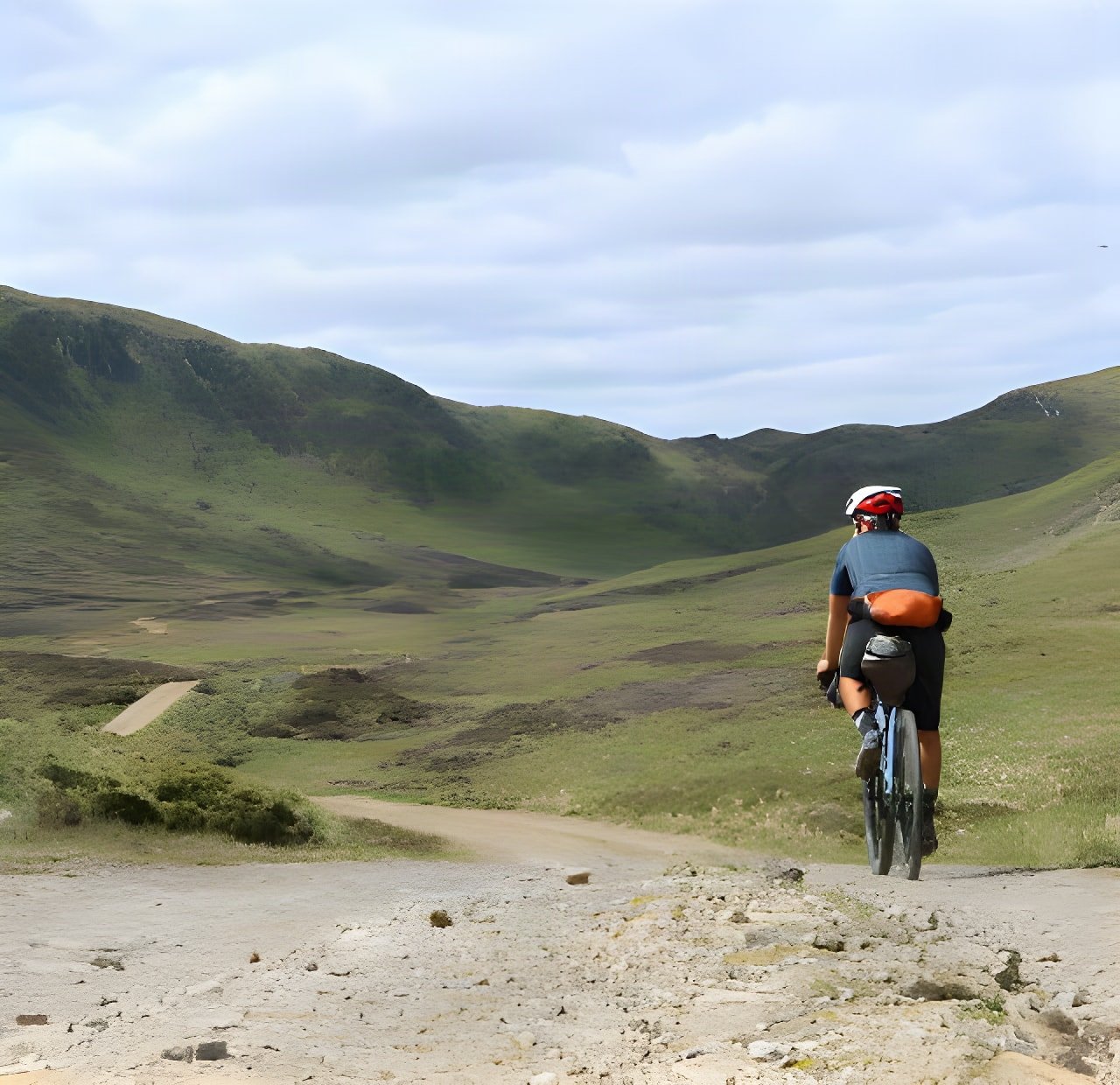 Bikepacker rides a gravel track through green hills on the Drovers Trail in Perthshire, Scotland.