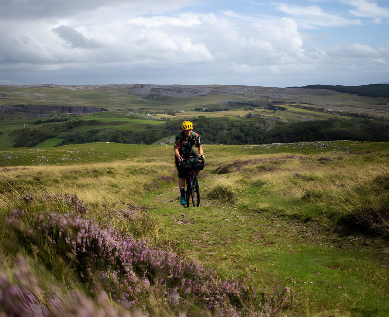 Bikepacker rides a grassy moorland track beside heather on the Black Mountain overnighter in South Wales.