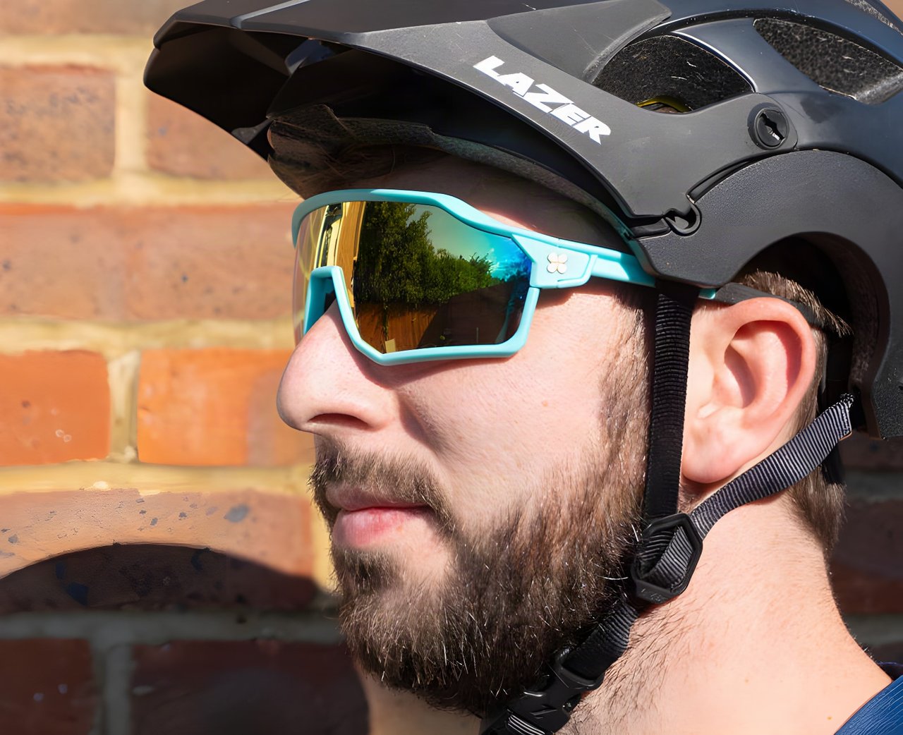 Rider in profile wearing minty-green SunGod Velans glasses with mirrored gold lenses under a Lazer helmet.
