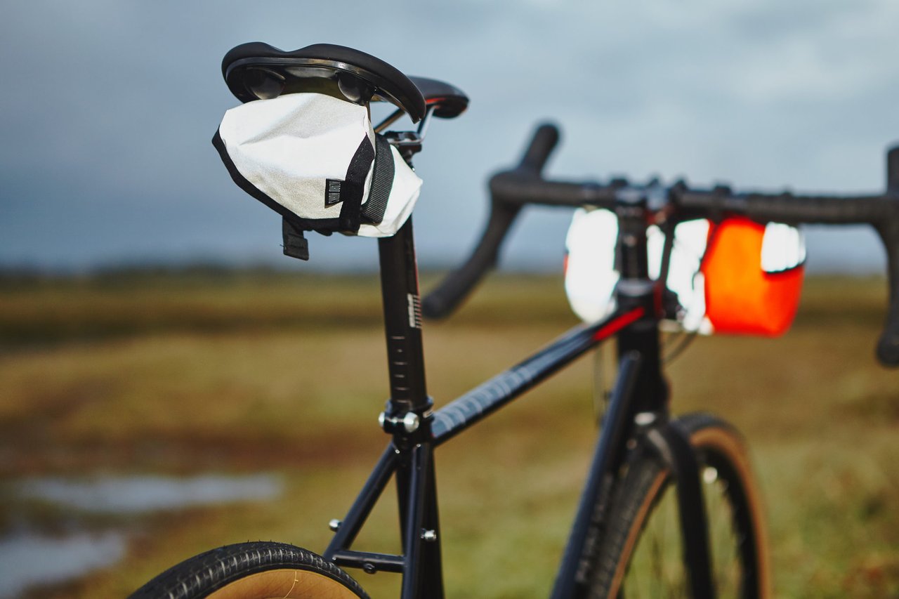 Wizard Works Wiz Viz reflective Teeny Houdini and Lil Presto! bags fitted to a black gravel bike in a wet field.