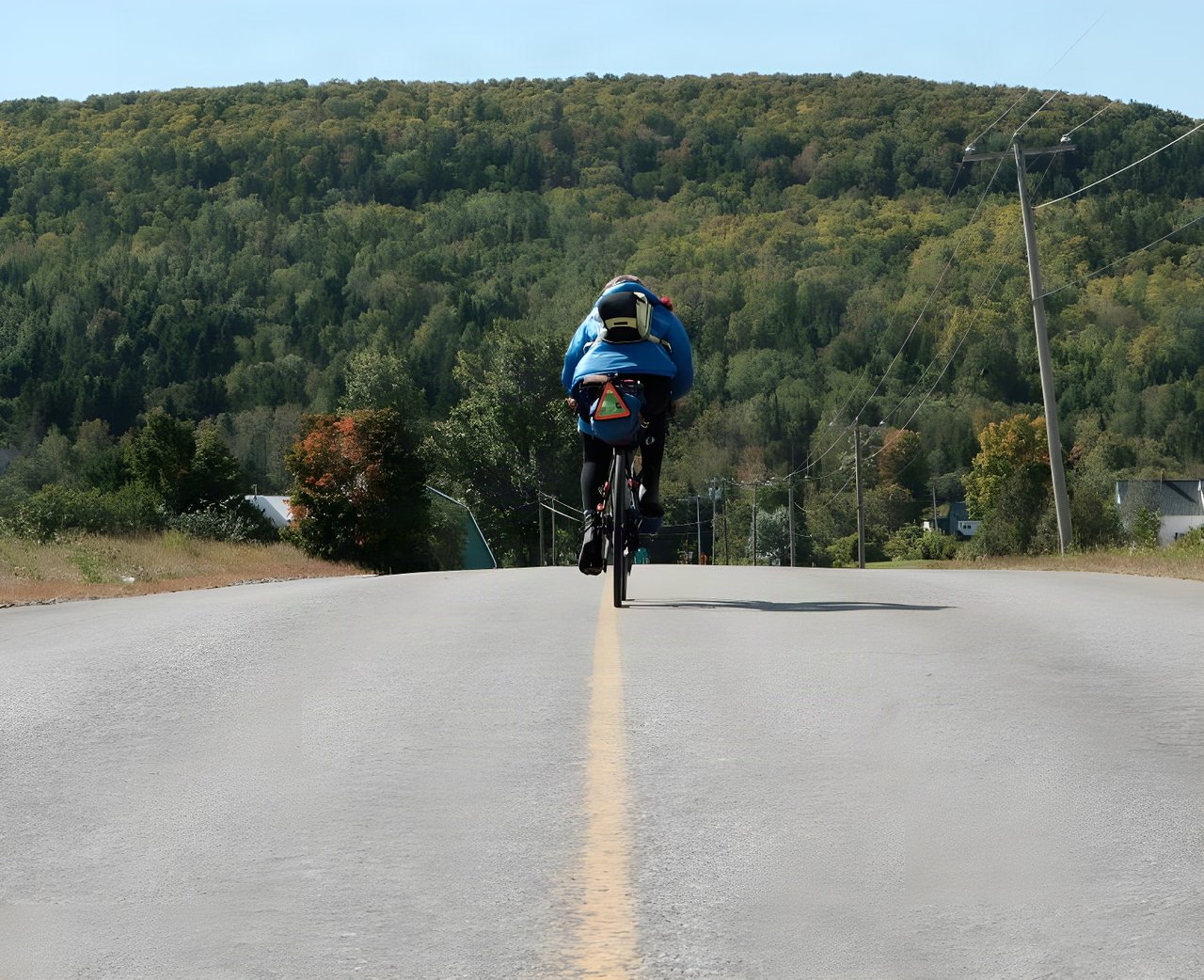 Loaded bikepacking rider on a quiet road below autumn woodland, from Vedangi Kulkarni's round-the-world ride.