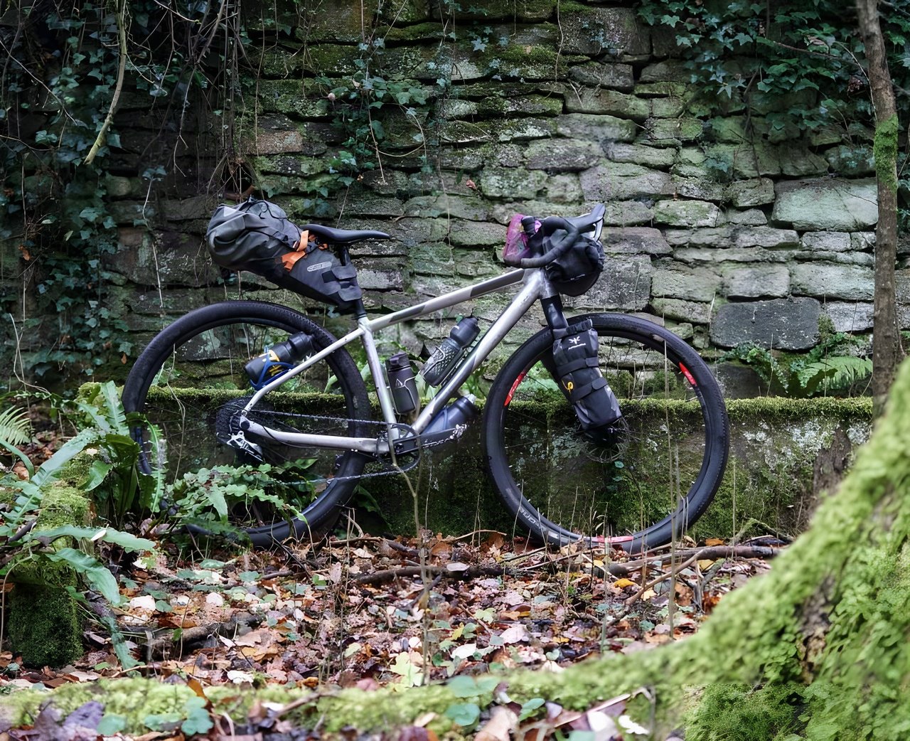 Riverside 920 bikepacking bike loaded with seat pack, bar bag and fork packs, leant against a mossy stone wall.