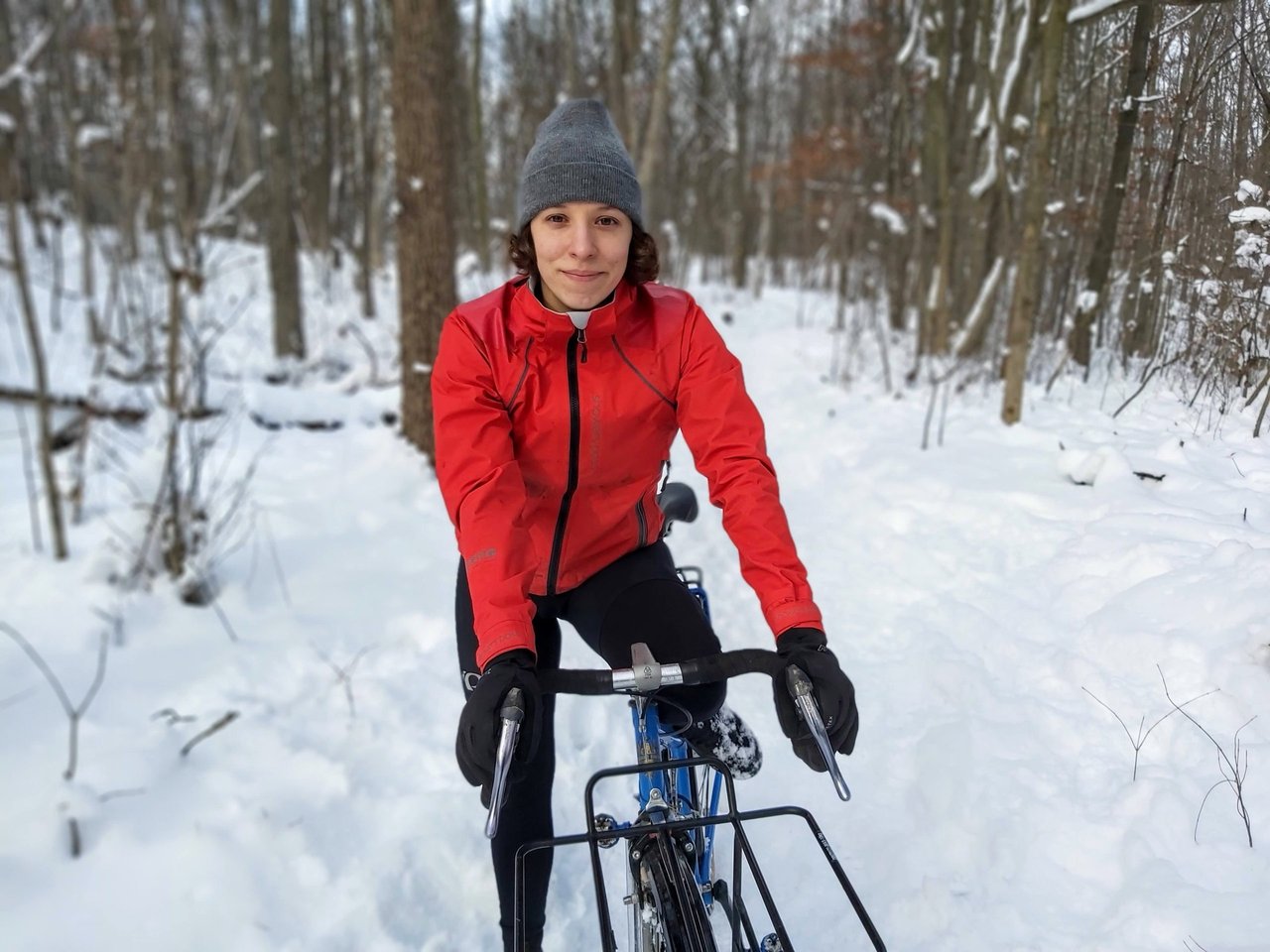 Rider in the red Showers Pass Refuge jacket on a drop-bar bike with a front rack in snowy Ontario woods.