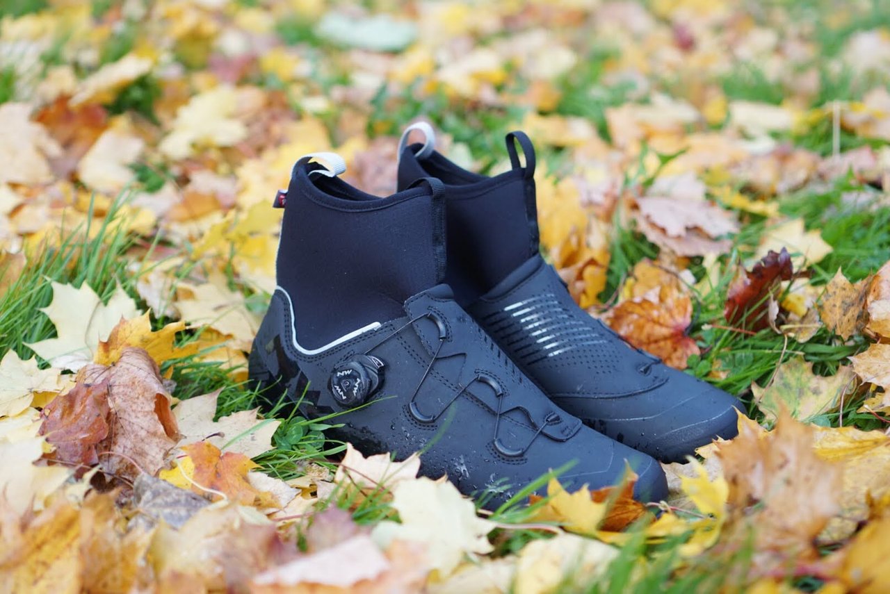 Pair of black Northwave Magma XC Core winter cycling shoes standing on autumn leaves, with neoprene cuffs and dial closure.