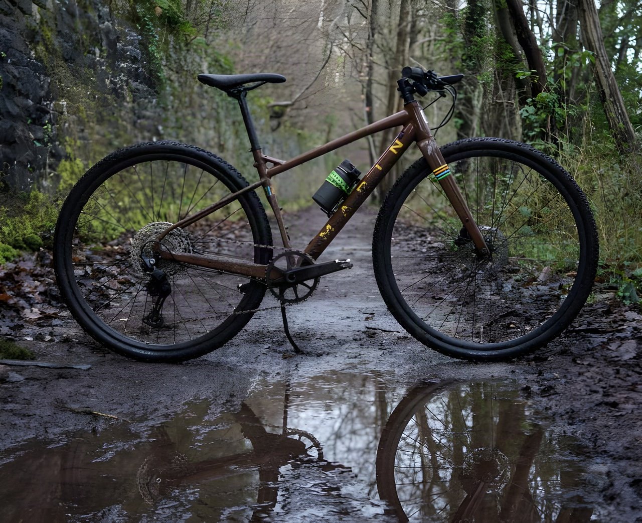 Marin DSX 2 flat bar gravel bike in brown parked on a muddy wooded track beside a puddle.