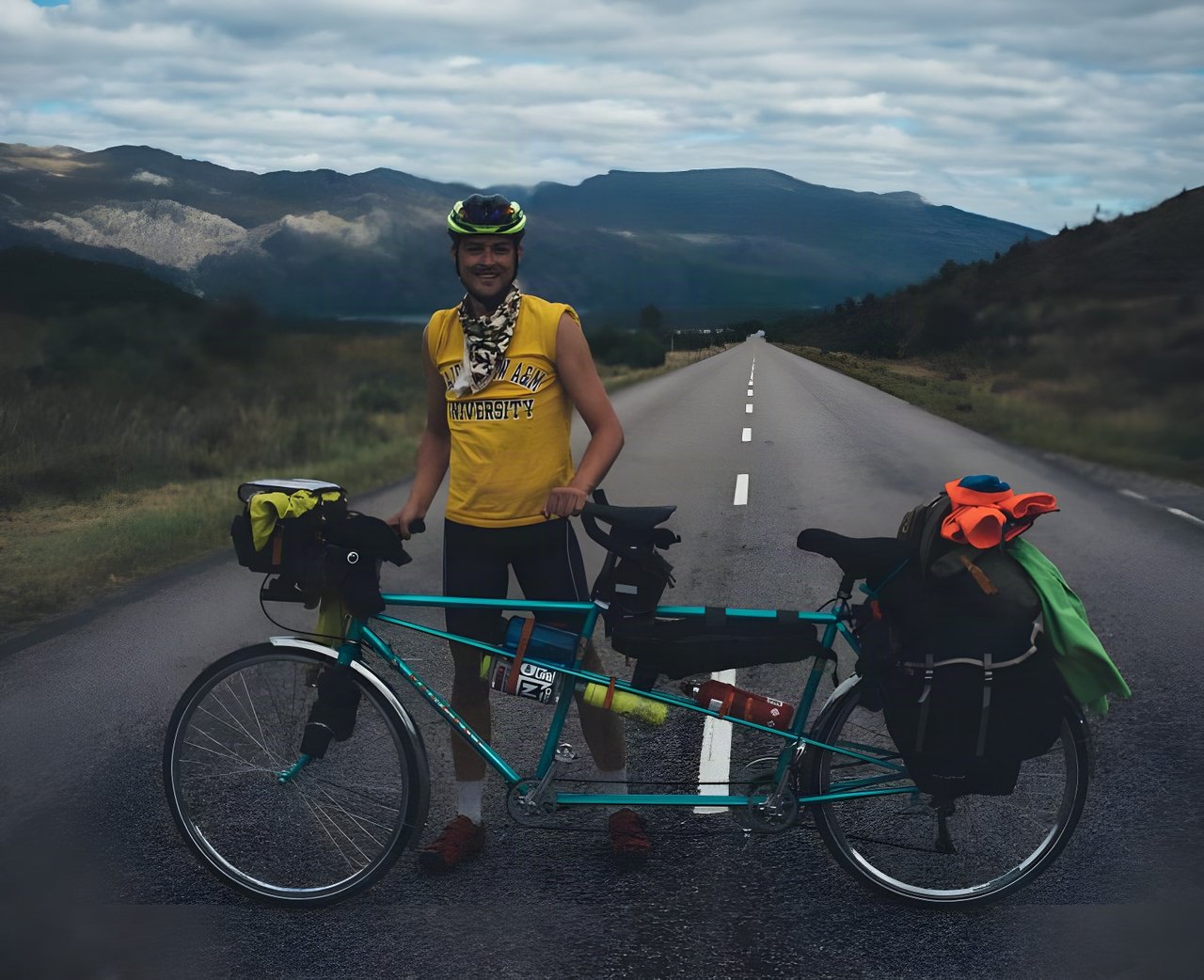 Rider stands beside a loaded teal tandem on an empty road in the Scottish Highlands on the NC500.