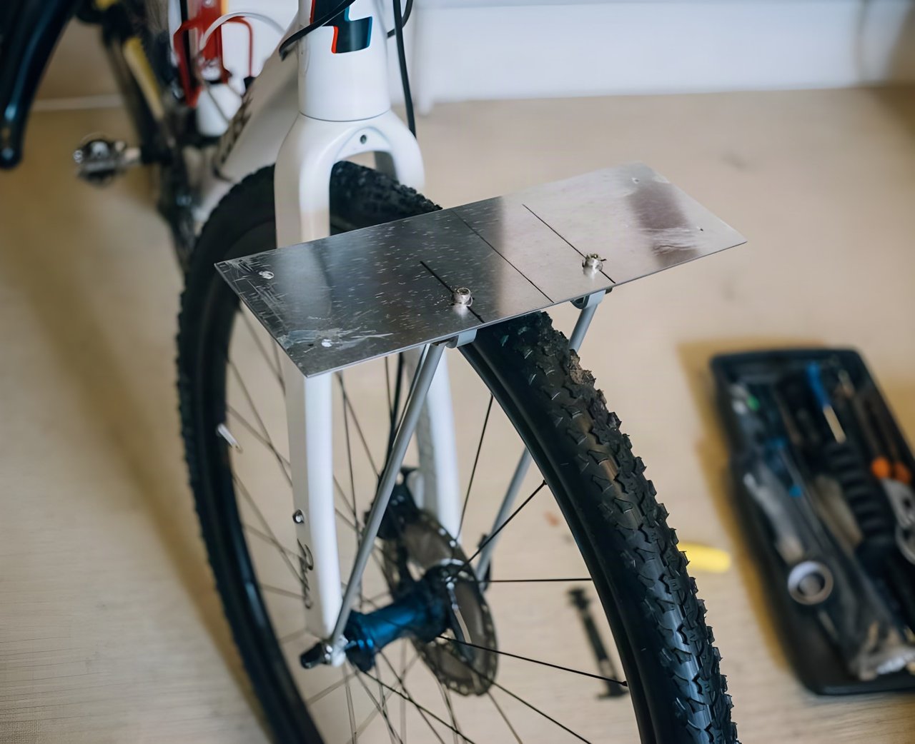 DIY front bag support made from an aluminium plate and Tubus struts, mounted above a bike's front tyre.