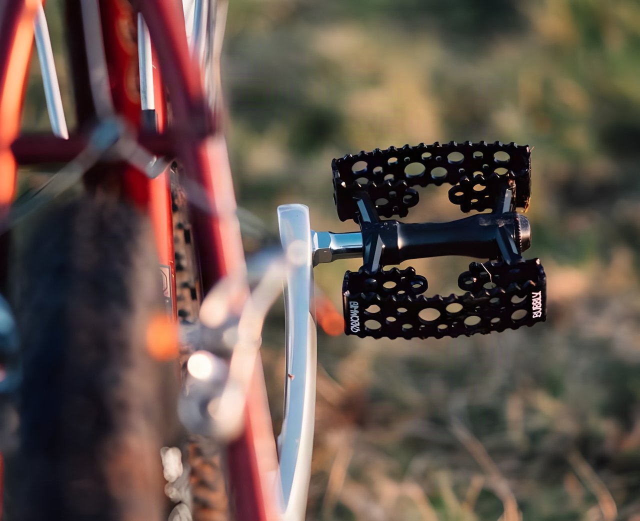 SimWorks Bubbly pedal by MKS, a black perforated double-cage flat pedal, fitted to a red bike in low warm sunlight.