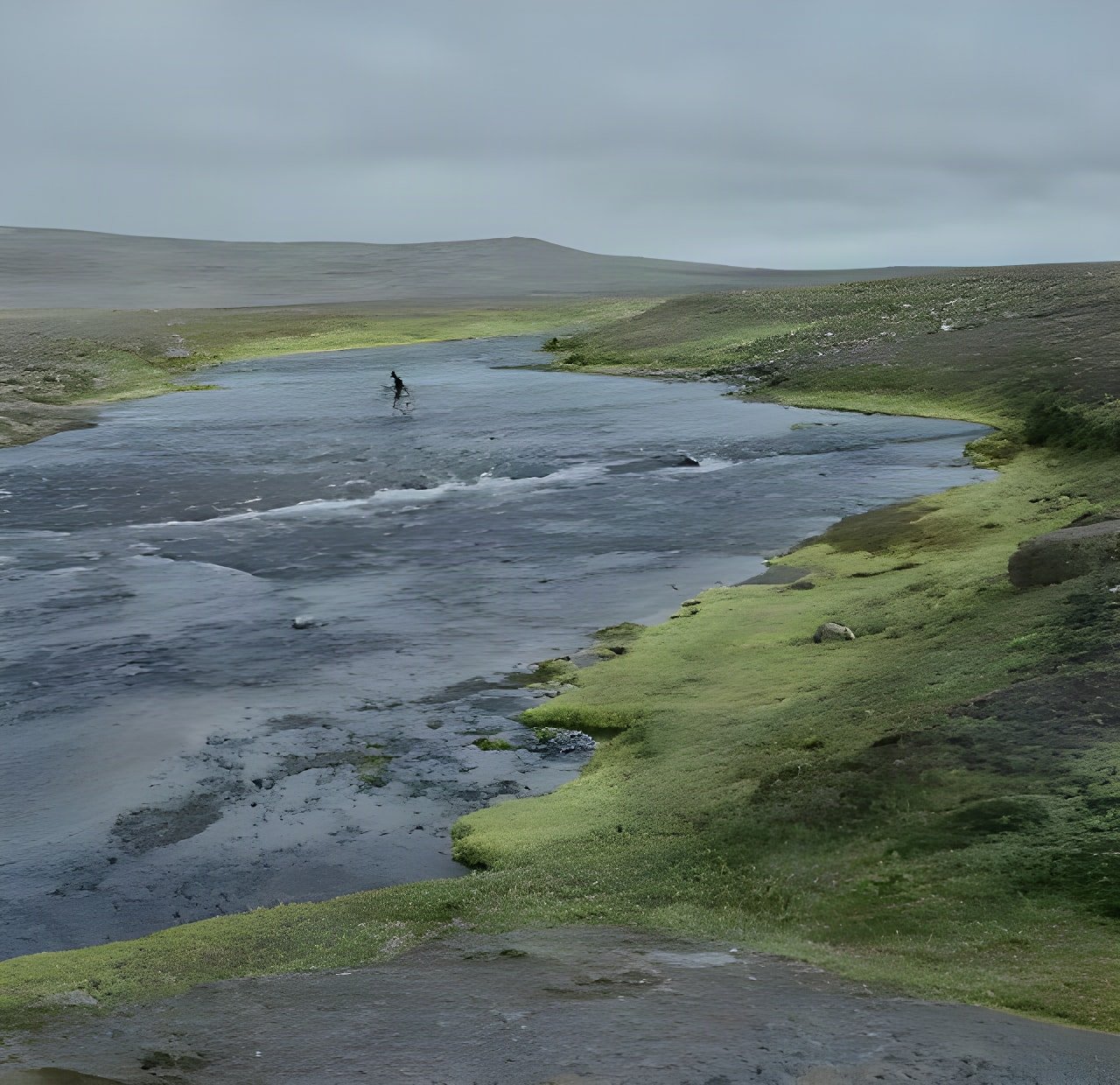 Lone cyclist wades a wide grey river on the Sprengisandur plateau in Iceland during Rapha's 2015 crossing attempt.