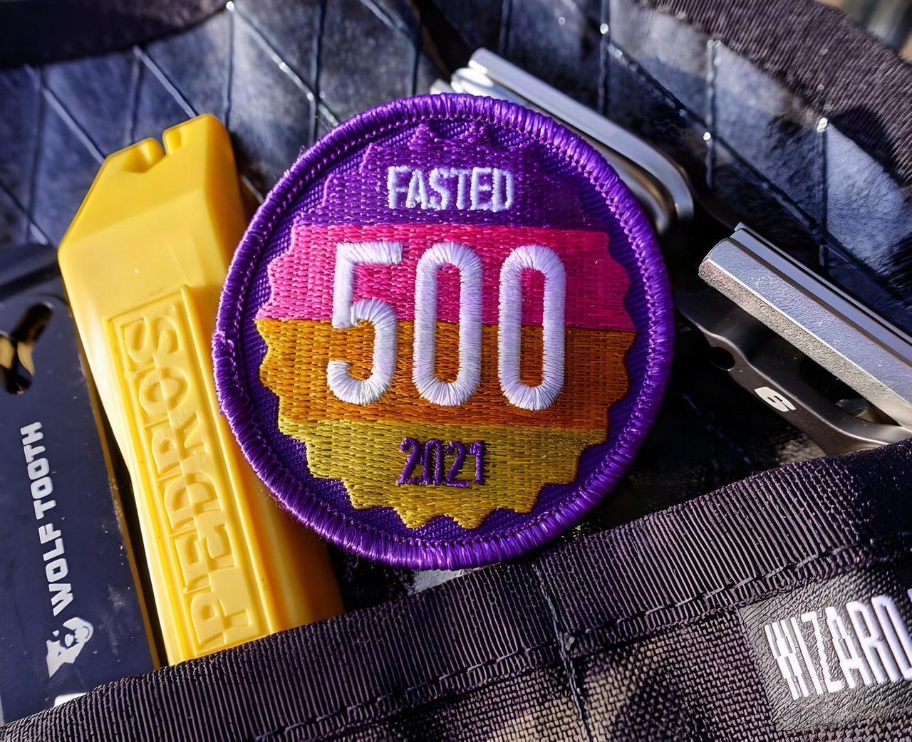 Fasted 500 2021 embroidered roundel in purple, pink, orange and yellow, laid among bike tools and a tool roll.