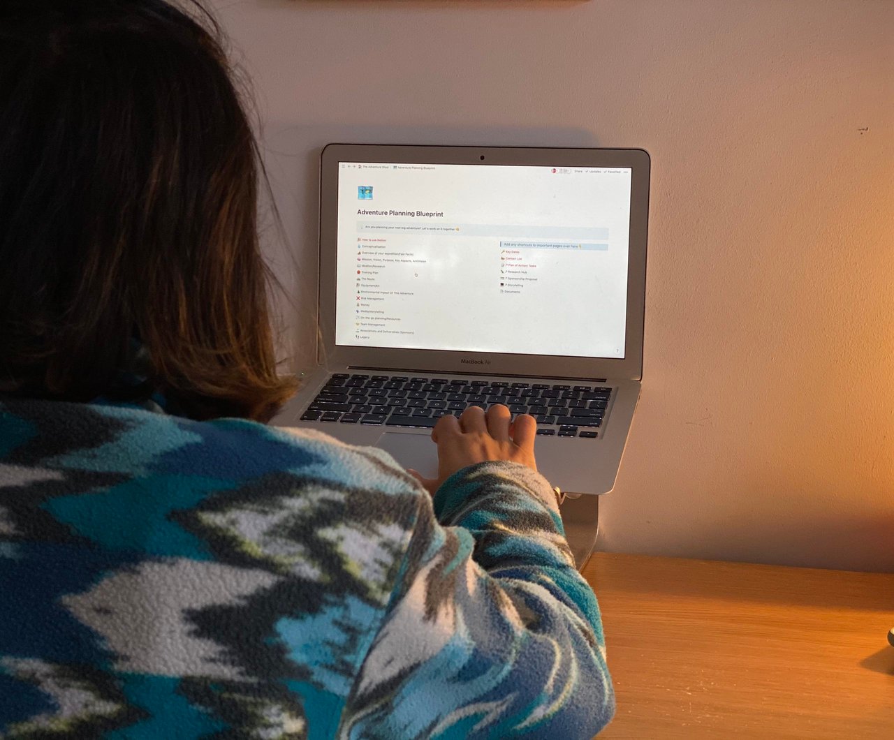 Adventure Planning Blueprint open in Notion on a laptop as a person in a patterned fleece works at a desk.