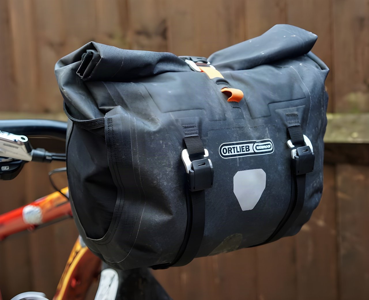 Ortlieb Handlebar Pack QR roll-top bar bag, in black with orange tab, fitted to a flat-bar bike.