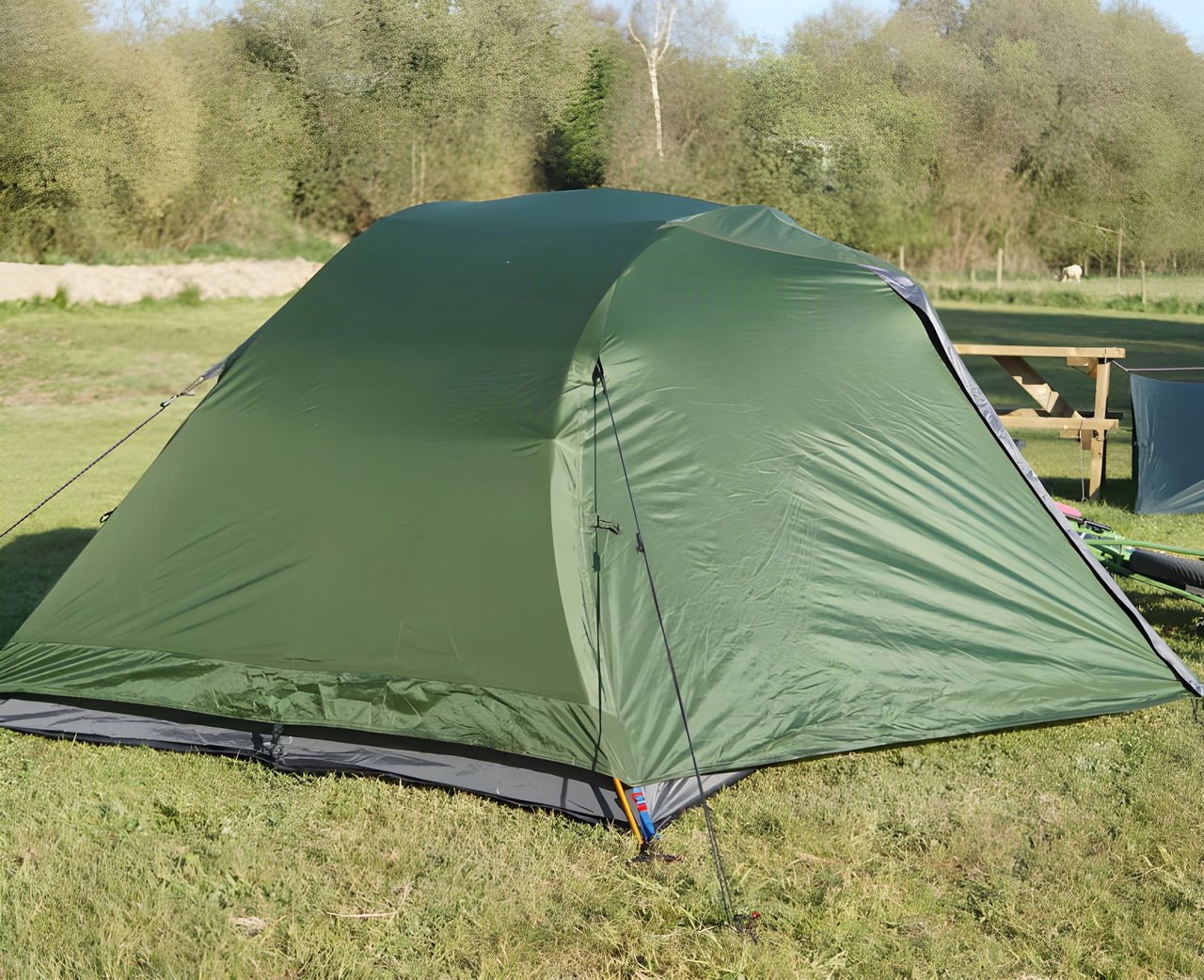 Green Alpkit Jaran 2 person tent pitched on grass beside a picnic bench in low sunlight.