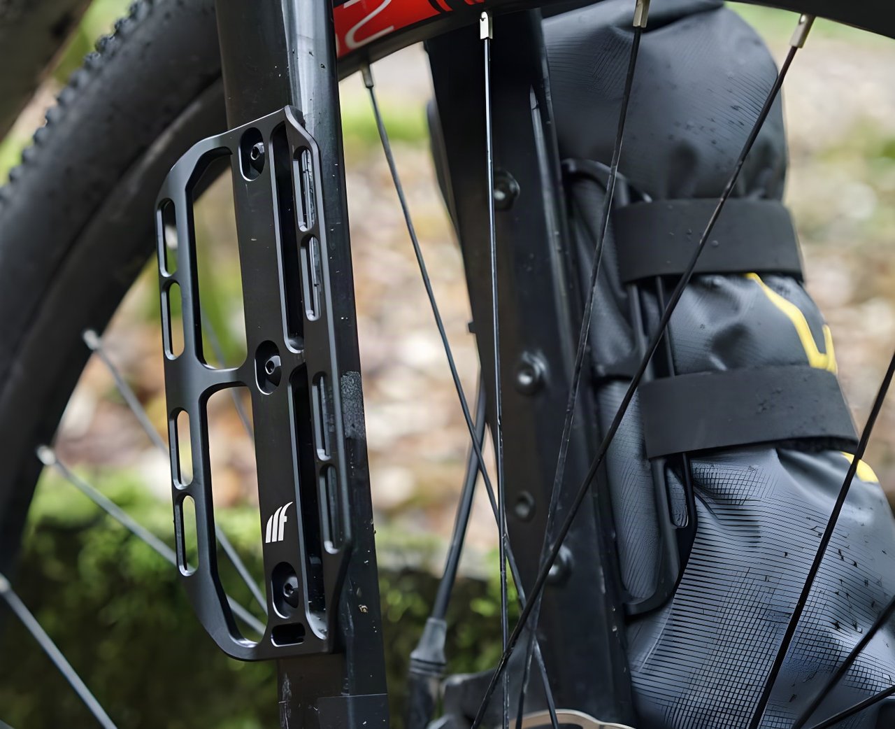 Close-up of a black Tailfin Cargo Cage bolted to a fork leg, next to a strapped-on Apidura fork pack.