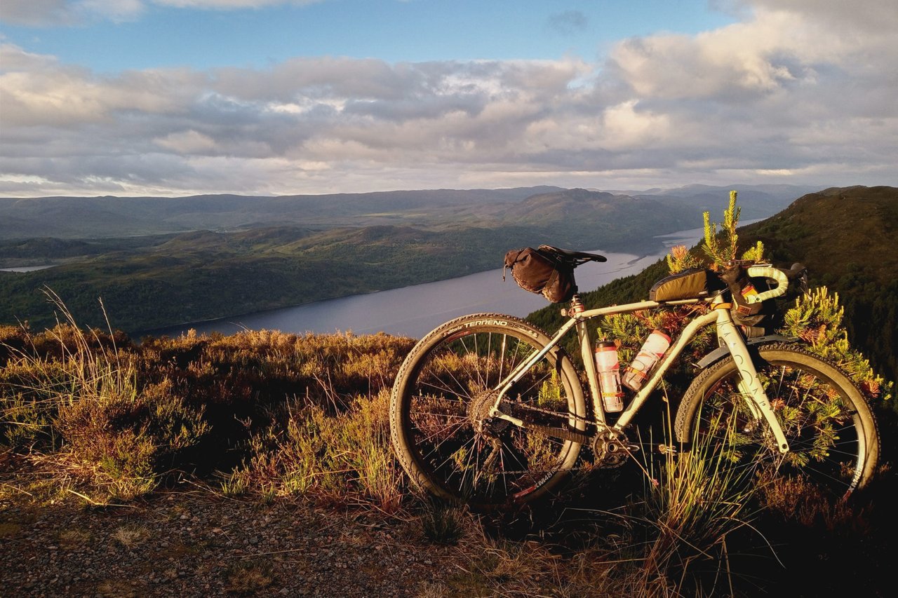 Loaded gravel bike on a heather hillside above Loch Ness in low sun, on the Badger Divide route in Scotland.