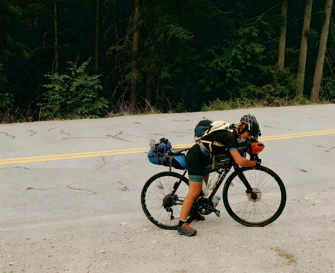 Silk Road Mountain Race interviewee Vedangi Kulkarni rests over the bars of her loaded bike on a forest road.