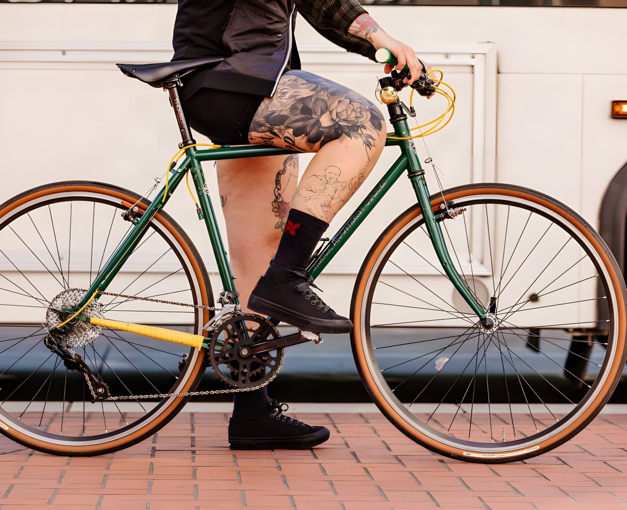 Cyclist with tattooed legs sits astride a green bike in black Chrome Industries x Panaracer Pedal Series trainers.