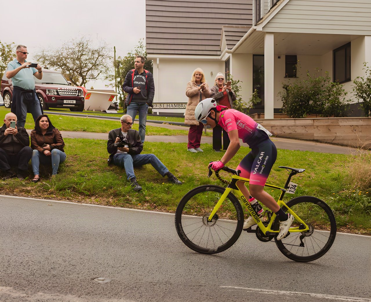 Women's Tour of Britain rider in pink on a yellow Cannondale climbs Hambro Hill past roadside spectators.