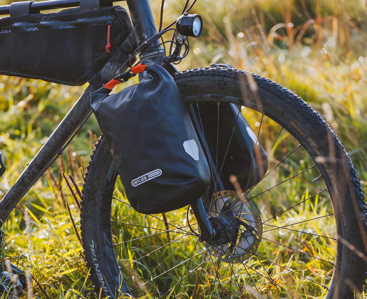 An Ortlieb fork pack mounted on a bike's fork among grass
